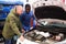 Worried client talking with specialist about repairing his car engine at workshop