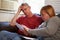 Worried Couple Sitting On Sofa Looking At Bills