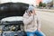 A worried driver is seen holding his mobile phone and standing alone next to his broken down car