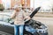 A worried driver is seen holding his mobile phone and standing alone next to his broken down car