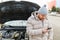 A worried driver is seen holding his mobile phone and standing alone next to his broken down car