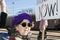 Worried looking senior citizen woman with colorful clothing and peace earrings at war protest with sign