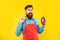 Worried man in apron showing OK gesture holding eggplant yellow background, shopkeeper