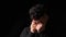 Worried man holding and covering his face with his hands while standing over a dark background.