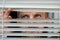 Worried man looking looks scared in window peeking out from blinds due to quarantine