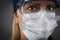 Worried Medical Worker Wearing Protective Face Mask and Gear Against Dark Background