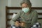 Worried middle aged woman 50s with grey hair and protective mask checking online news with mobile phone during covid-19 virus home