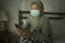 Worried middle aged woman 50s with grey hair and protective mask checking online news with mobile phone during covid-19 virus home