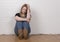 Worried and upset female sitting against a white brick wall