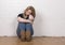 Worried and upset female sitting against a white brick wall