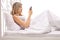 Worried woman lying in bed and looking at a mobile phone