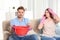 Worried young man collecting water leakage from ceiling while his wife calling plumber