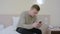 Worried young man typing an sms message on his cell phone sitting on bed at home