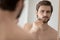 Worry young handsome man examining face in mirror reflection