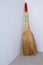 A woven sorghum broom stands in the corner of a room with gray plastered walls. Cleaning the house