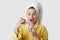 Wow, is it for me? Glad overjoyed European woman looks happily, holds cream, wears towel and bathrobe, cares of appearance, puts
