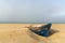 Wreck of an old wooden rowboat buried in the sand with an overcast sky and ocean behind