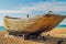 A wrecked hull rests on the shore on a bright sunny day with a seagull sitting on the prow.