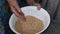 Wrinkled hand over bowl full of raw buckwheat groats