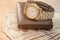 Wristwatch on a wallet and dollars on a wooden table. Close-up. Image is tinted.