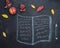 Writing pad or copybook and pen hand drawn in chalk on a blackboard with autumn leaves and apple.