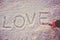 Written or drawn by hand in pink glove word LOVE on white snow