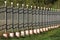 Wrought iron fence with vertical grey metal bars in a row mounted on concrete foundation surrounded with grass and fallen leaves