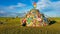 Xilinhot -A woman in a beanie sitting on a vast pasture under a heap of stones (aobao) with colorful prayer flags attached to it.