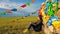 Xilinhot -A woman in a beanie sitting on a vast pasture under a heap of stones aobao with colorful prayer flags attached to it.