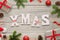 Xmas white letters on wooden table surrounded with Christmas decorations, gifts, fir branches, balls, Santa hat and pinecones