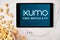 Xumo on the screen of the tablet with popcorn box and Apple earphones on the background. Application for searching free