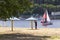 The yacht floats on the river along the city. A man stands on the beach under an umbrella from the sun