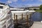 The yacht is moored at the pier of the river, near a wooden bridge. Part of the frame.