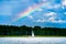Yacht with white sail on a lake against gloomy rainy blue sky and the rainbow
