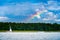 Yacht with white sail on a lake against gloomy rainy blue sky and the rainbow