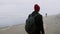 Yang man in red hat is walking alone across the beach in autumn.