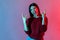 Yeah, that`s crazy! Neon light portrait of delighted happy woman showing rock and roll hand gesture, punk sign