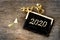 Year 2020 written on a black little sign  with golden glitter and ribbon on wooden background