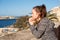 A yearning girl standing and praying makes a wish near the parapet over the sea water on a bright sunny day