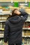 Yekaterinburg, Russia - November 2019. A man in thought in front of the rows of alcohol in a supermarket. A wide range of