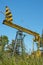 A yellow abandoned oil rig against a background of green grass and blue sky. The concept of the decline of the oil