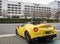 A yellow Alfa Romeo sportscar drives out of a car park