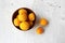 Yellow apricots with a clay bowl on a white wooden background.