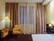 Yellow armchairs and a luminous floor lamp stand in the corner of the room near the window with curtains. Hotel room