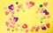 Yellow background with colorful cut out and candy hearts in mostly pinks and purples and a few tiny flowers - Room for text