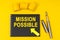 On a yellow background lies a pen, a black notebook with the inscription - MISSION POSSIBLE