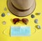 On a yellow background, a summer hat, sunglasses, a medical mask and seashells