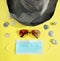 On a yellow background, a summer hat, sunglasses, a medical mask and seashells