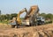 Yellow backhoe digging soil fill in rear truck