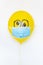 Yellow balloon with medical mask and doodle eyes. Conceptual image of Birthday party during Corona virus quarantine